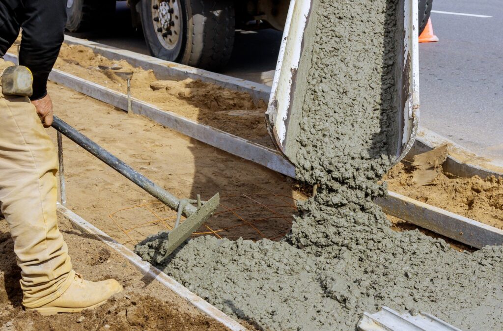 Concrete being poured from a mixer truck into a concrete with sidewalk