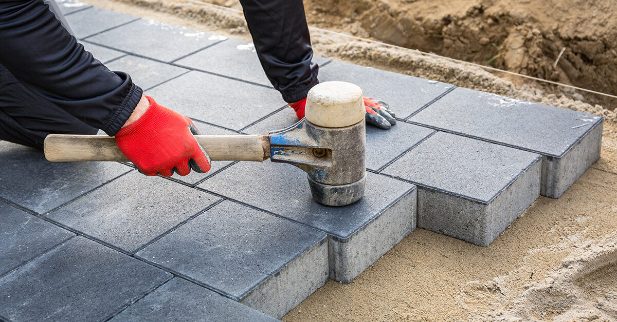 Craftsman installing grey permeable pavers on a new driveway