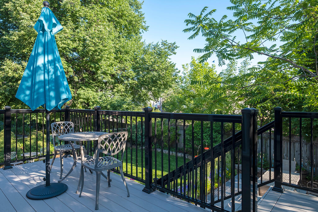 Gray PVC decks with black metal railings, featuring a bistro set and blue sun umbrella in a backyard.