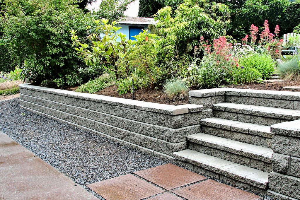Close-up of a retaining wall with staircase, made of gray concrete blocks, in a garden landscape.