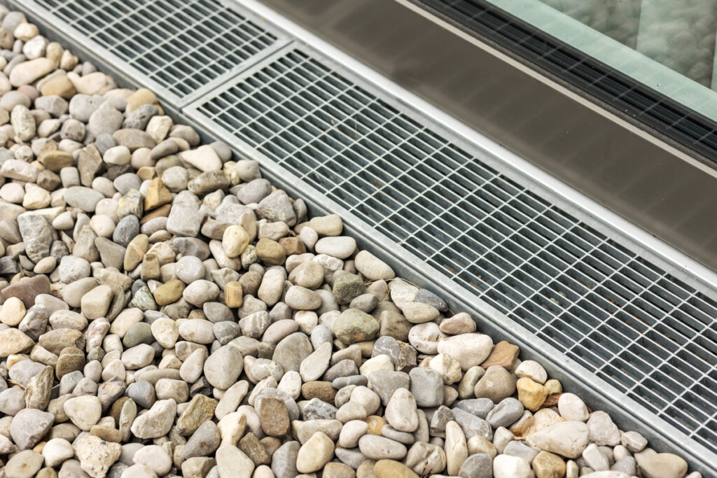Stainless steel drain box surrounded by pebbles, with a gravel floor and French drain
