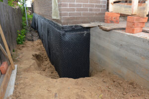 Waterproofing contractor installing dimple mat and drain in a basement corner with rigid foam board insulation.