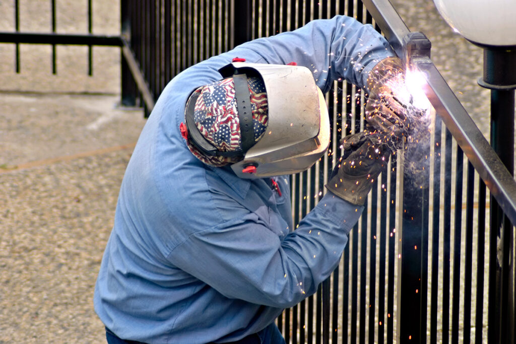 Welder installing a new wrought iron fence